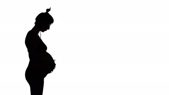 LEFT SILHOUETTE, A heavily pregnant woman looks down and strokes her belly