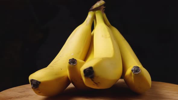 Close-up of ripe yellow bananas on a wooden surface spinning against a dark background
