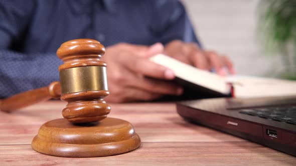 a Gavel on Table with Young Man Reading a Book on Background