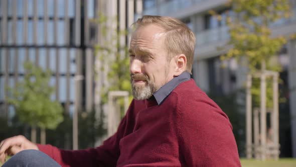 A Middleaged Handsome Caucasian Man Looks Around As He Sits in a Street in an Urban Area