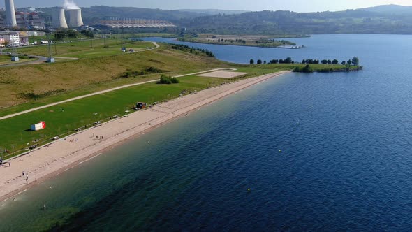 people enjoying the lake beach thermal power plant with gardens and clean water on a sunny afternoon