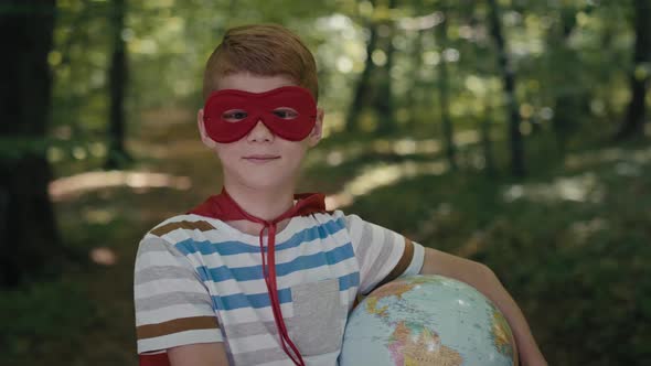 Portrait of ginger boy with superhero costume holding globe in the forest. Shot with RED helium came