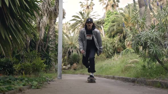 Young Skater skating in garden walkway with palmtrees, tracking shot