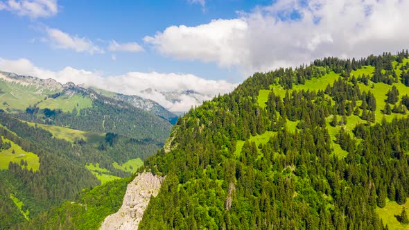 Stunning aerial hyper lapse of green mountains with white clouds rolling through a clear, blue sky