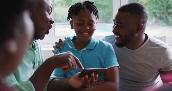 African american grandfather, father and son smiling while using smartphone together at home