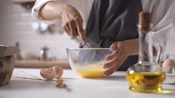 Cooking Dough In The Kitchen. Cooking. The Chef Beats The Eggs In A Bowl With A Whisk. A Girl Beats