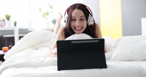 Smiling Woman in Headphones Communicates By Video Call While Lying in Bed