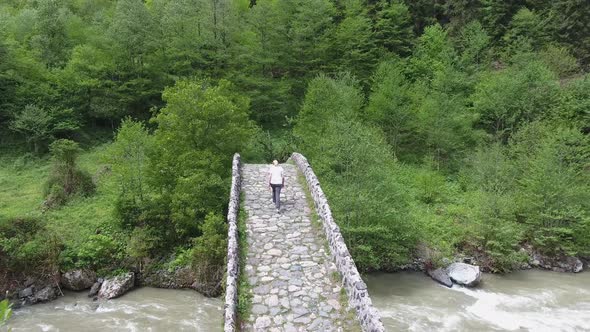 Woman Walking on Historic Stone Bridge in Spring Forest