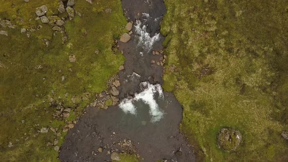 Aerial top down dolly out of river and Glymur waterfalls streaming down rocky cliff in verdant highl