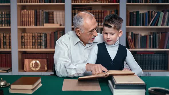 Caring Grandfather and Kid Grandson Reading Literature Textbook at Library Together