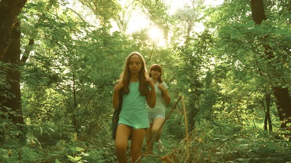 Happy Girls Travelers with Backpacks Go Through the Thicket in the Forest. Children Tourists Travel