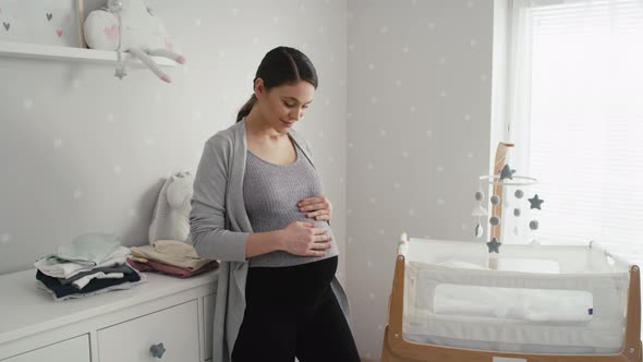 Thoughtful caucasian woman in advanced pregnancy standing in the baby's room next to the crib. Shot