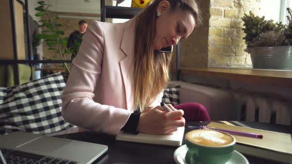 Pretty Woman Wearing Casual Suit Talking on the Mobile Phone and Sitting in Coffee House, Working