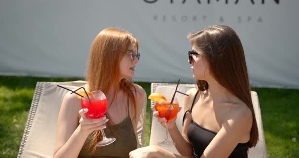 Two Girls in Swimsuits with Cocktails Resting on Sun Loungers