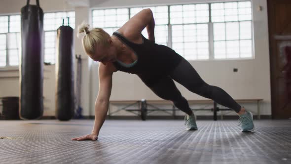 Fit caucasian woman performing one handed push up exercise at the gym