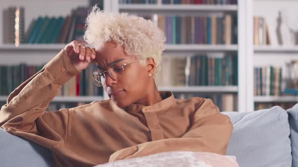 Young African American Woman Has Health Problems Feels Pain in Head Sits on Sofa