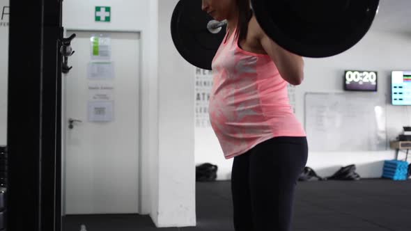 Footage of a pregnant female model doing squats in a gym trying to keep fit in her fourth trimester