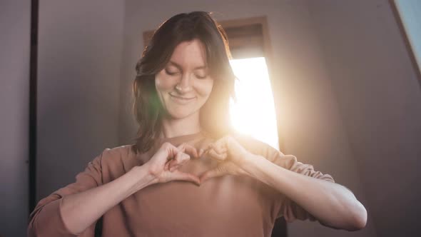 A beautiful girl blows a kiss and shows her heart to the camera.  doing shape of hear. Flirting.