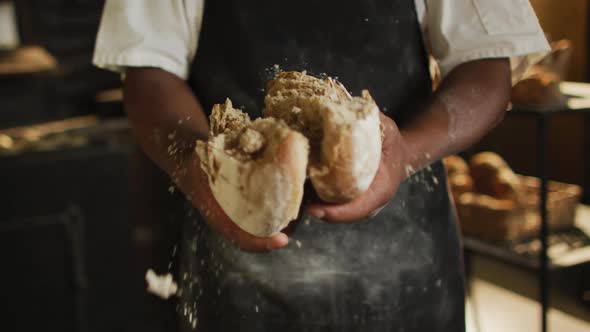 Animation of hands of african american male baker opening freshly baked bread