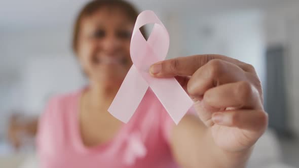 Smiling african american senior woman wearing pink t shirt holding pink breast cancer ribbon