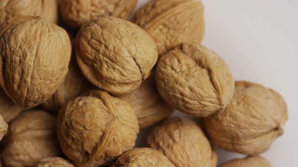 Cinematic, rotating shot of walnuts in their shells on a white surface 