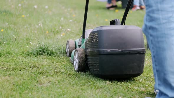 Cropped View of Lawn-mover and Legs on Grass in Village