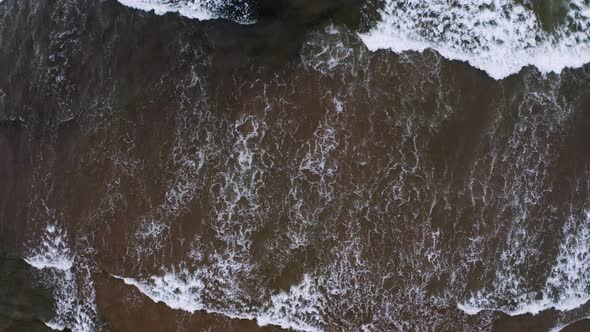 Aerial top-down view of waves and whitecaps approaching the beach on a windy day.