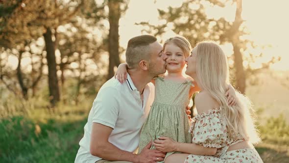 Young married couple with cute little girl spend time together outdoors during sunset.