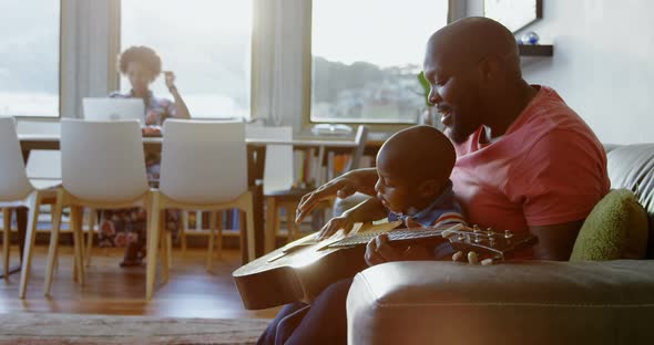 Father teaching his son how to play guitar at home 4k