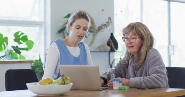 Female health worker and senior woman discussing over laptop at home