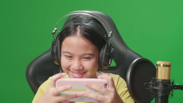 Excited Asian Kid Girl Playing Video Game With Mobile Phone While Live Stream On Green Screen