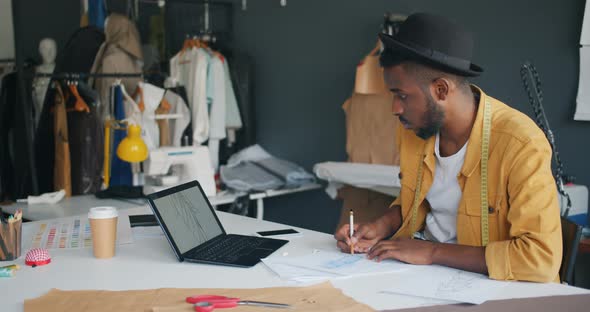 Clothes Designer Sketching Looking at Laptop Screen Working Alone in Studio