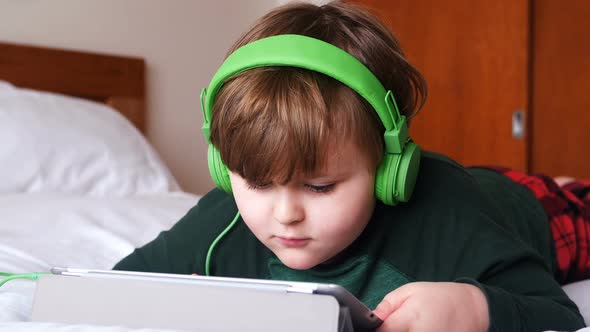 Boy in headphones using digital tablet in bedroom 4k