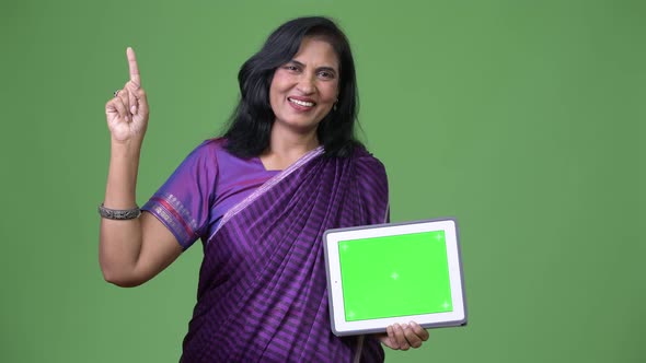 Mature Happy Beautiful Indian Woman Showing Digital Tablet and Pointing Finger Up