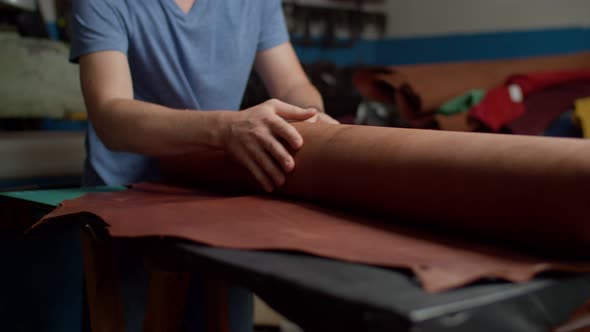 Closeup of Craftsman Hands Unfolding Leather Roll on Table Indoors