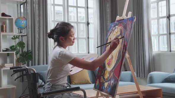 Asian Artist Girl In Wheelchair Holding Paintbrush Mixed Colour And Painting A Girl On The Canvas