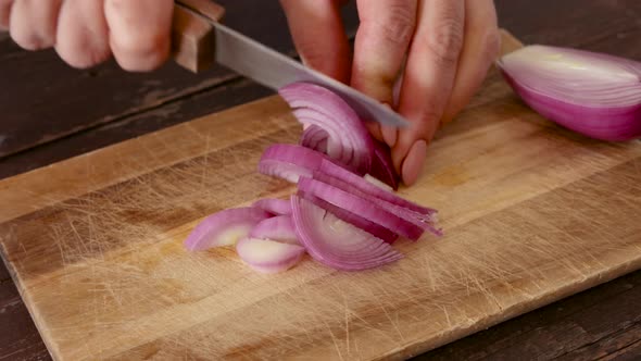 Woman's hands chopping fresh onion on a wooden board close up