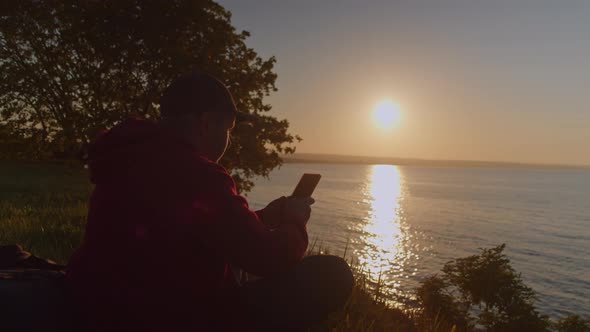 Man Uses a Smartphone While Sitting on the Seashore While Traveling