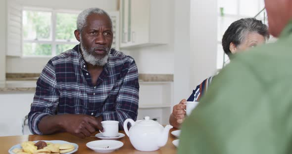 Two diverse senior couples sitting by a table drinking tea together at home