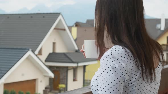 Young Woman Dreamily Watching on the Mountains and Drink Coffee or Tea From the White Cup