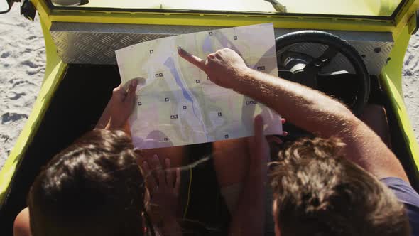 Caucasian couple standing near beach buggy by the sea reading a map