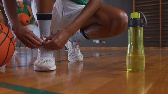African american female basketball player tying shoes with teammates in background