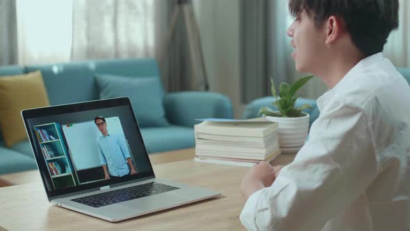 Asian Man Student Study With Teacher In Computer Screen While Learning Online At Home