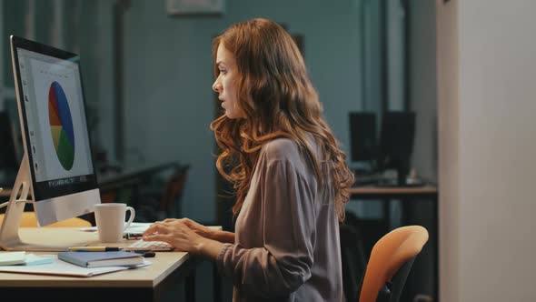 Surprised Business Woman Looking at Financial Report on Computer Screen at Night