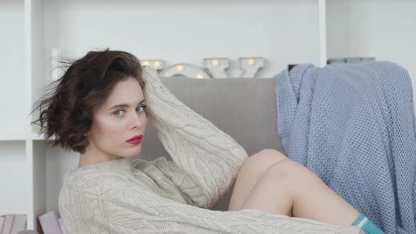 Portrait of Pretty Brunette Relaxing on Armchair and Smiling at Camera