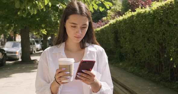 Young Woman with Take Away Cup and Drink Hot Coffee, Looking at Smartphone, Dressed in Business Suit