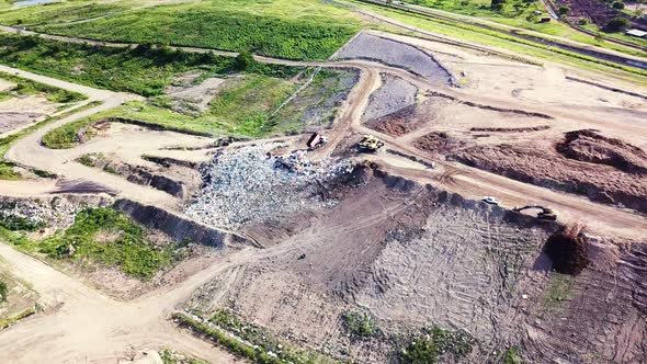 Drone circling in arc around large pile of rubbish at landfill site, surrounded by green vegetation.