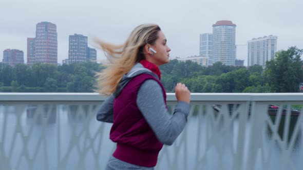 Woman is Running on the Bridge with Wireless Earphones