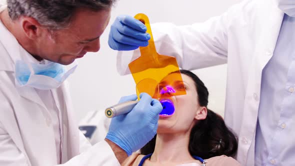 Dentists examining female patient with dental curing light