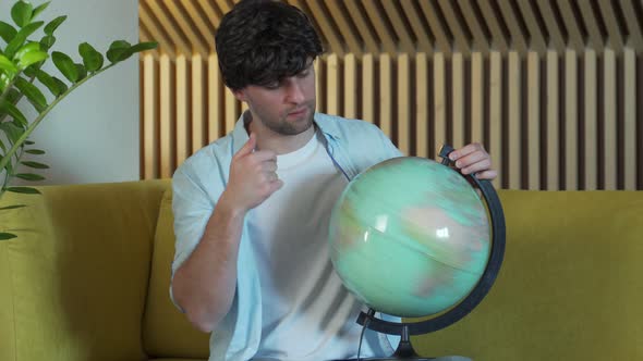 Man Looking for Countries on Globe at Home in Living Room on Sofa